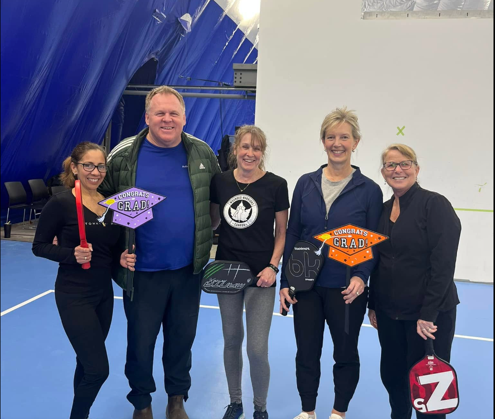 Group of five pickleball players graduating from kingston racquet centres beginner program with pickleball authority paddles on a blue indoor court.